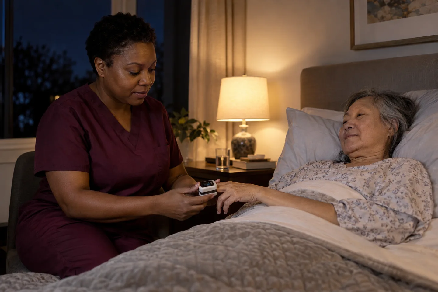 Illustrative scene: A female nurse in plum scrubs checks on an older woman beside a softly lit bed at night
